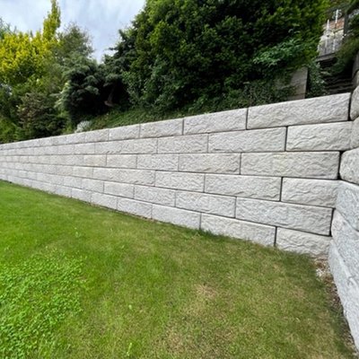Lange Stützmauer aus hellen Betonsteinen sichert den Hang im Garten – mehr nutzbare Fläche und weniger Pflegeaufwand