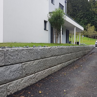 Betonmauer entlang der Einfahrt gleicht den Hang elegant aus und schafft klare Grundstücksgrenzen