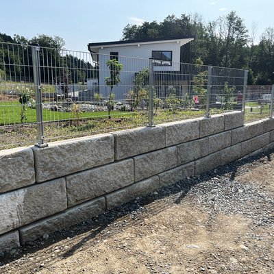 Betonmauer mit Zaun zur kombinierten Hangabstützung und Grundstücksbegrenzung