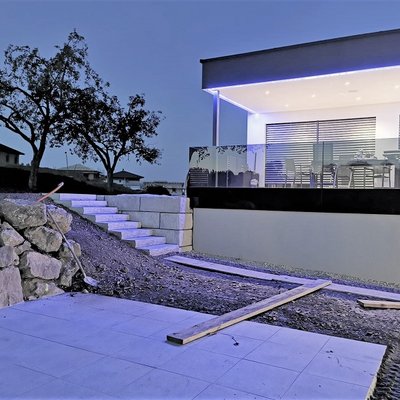 Dezente Betonmauer mit Stufen sichert den Hang und passt zur modernen Architektur des Hauses