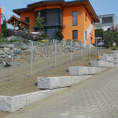 Stützwand aus Betonsteinen stützt die schräge Einfahrt und wirkt dabei modern und ordentlich