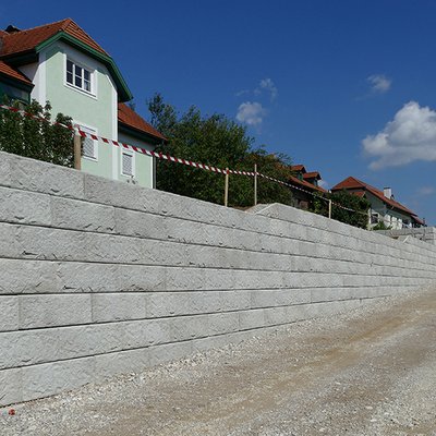 Massive Betonwand mit klarer Linienführung sichert das Gelände entlang der neuen Zufahrt