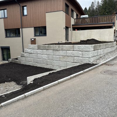 Terrassierte Gartenfläche mit strukturierter Betonmauer – platzsparende Lösung zur Hangbefestigung direkt an der Grundstücksgrenze
